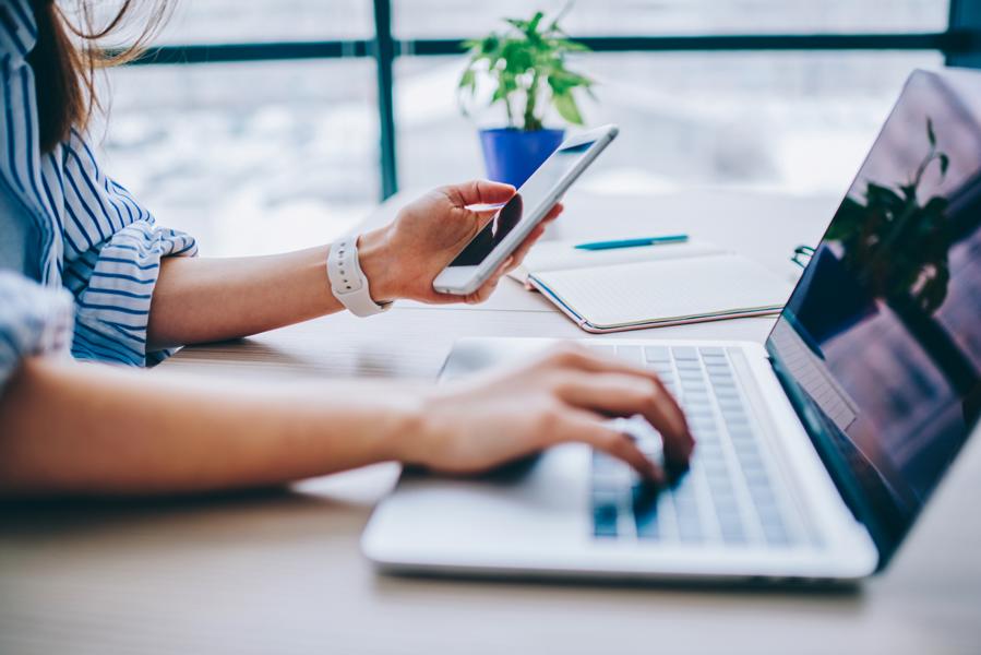 Frau arbeitet an Laptop und Handy gleichzeitig